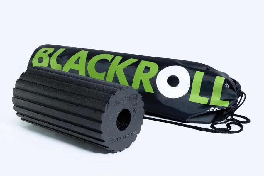 Sort foam roller med skrå savtakkede riller på overfladen, liggende foran en sort Blackroll-gymnastikpose